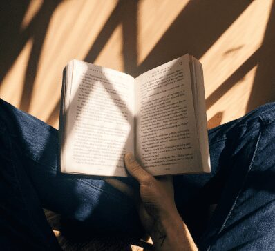 Person reading a book with sunlight and shadows on the pages.