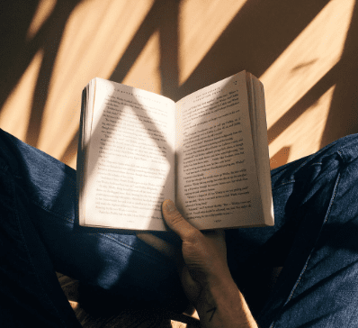 Person reading a book with sunlight casting shadows.