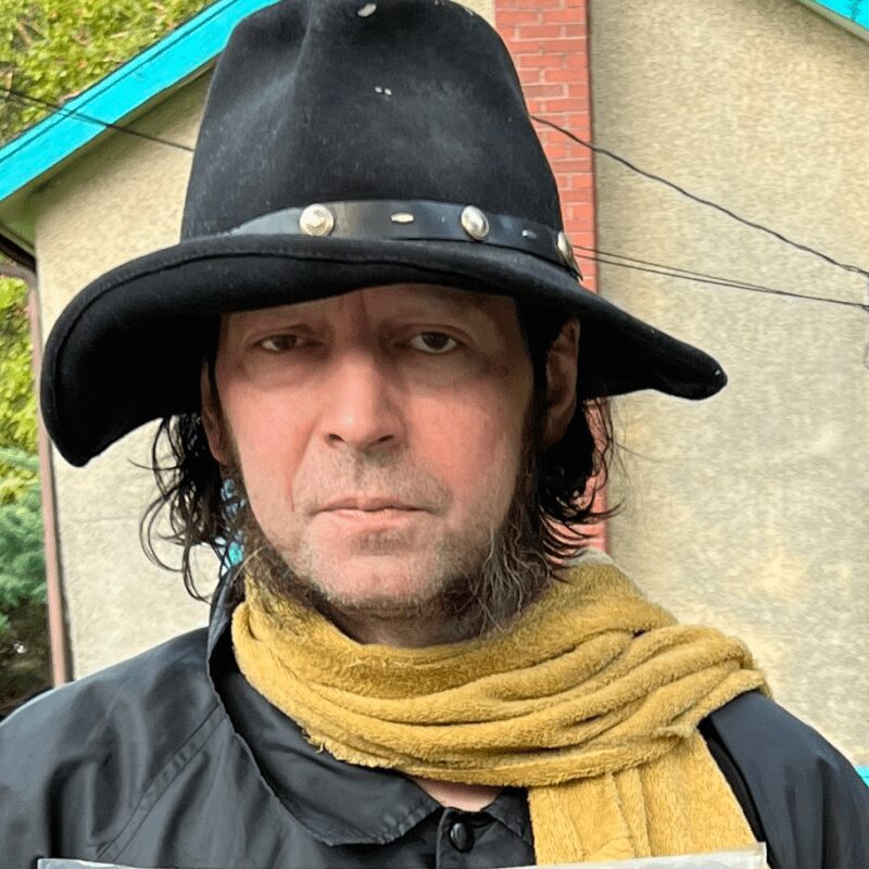 Man wearing a wide-brimmed black hat and a yellow scarf.
