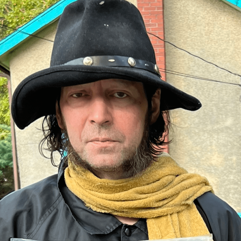 Man wearing a wide-brimmed black hat and a yellow scarf.